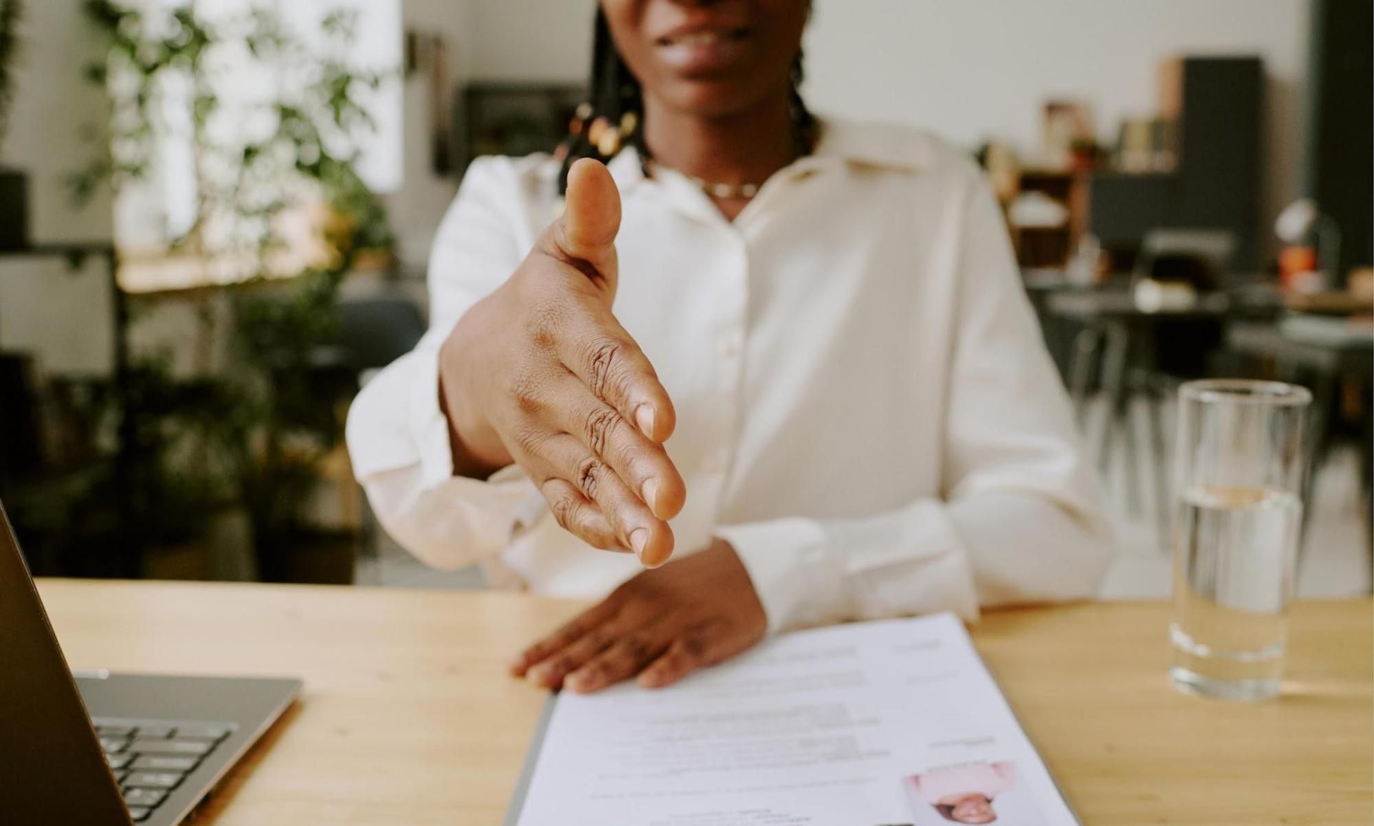 Interviewer extending handshake across desk