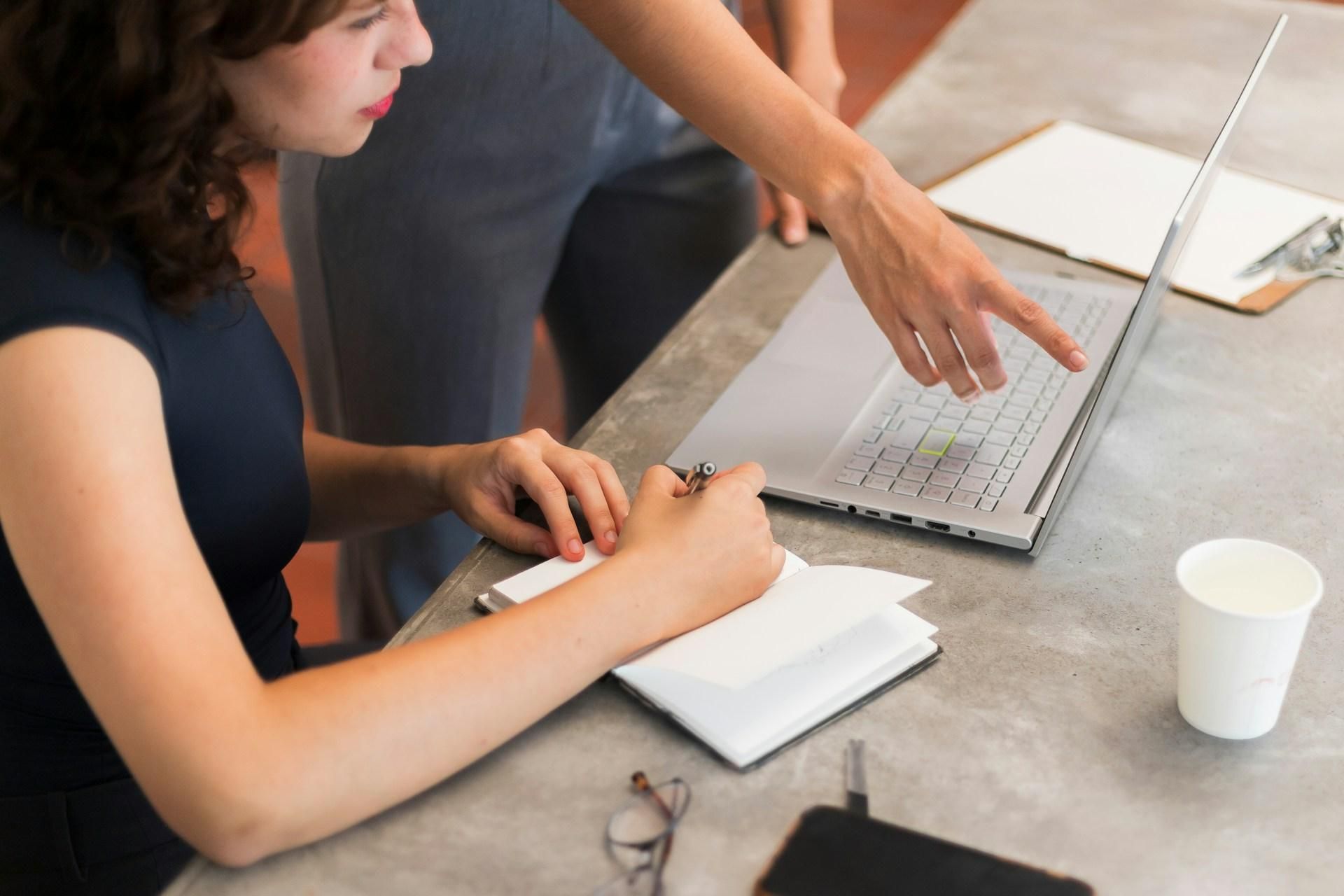 Mentor pointing at a laptop screen while a student takes notes, illustrating hands-on internship guidance
