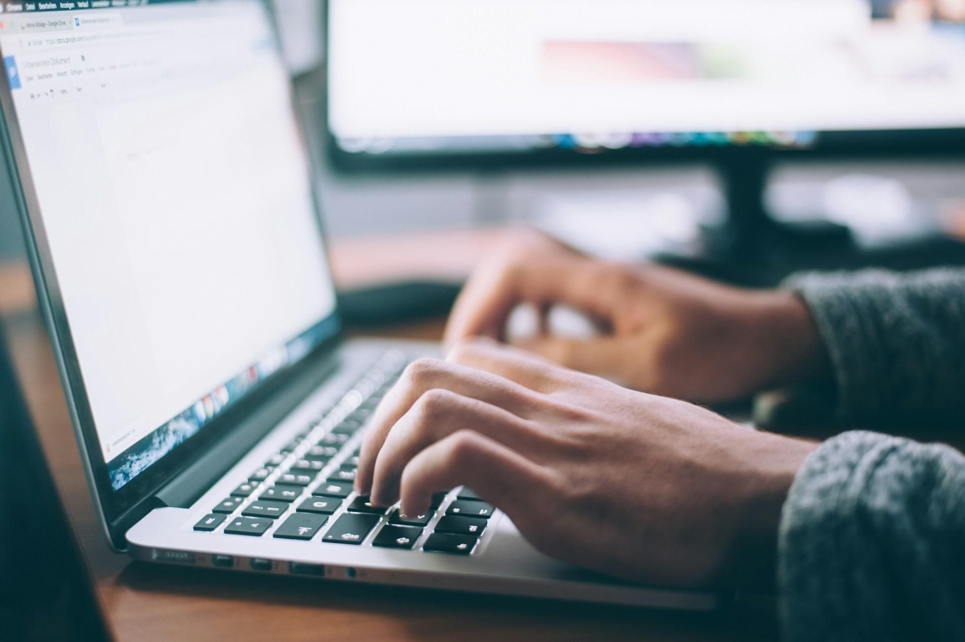 Student typing on a laptop with a dual-monitor setup, searching for internship opportunities online